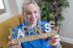 Telford Hall Care Home Carer Holding Sign that says Happiness Lives Here