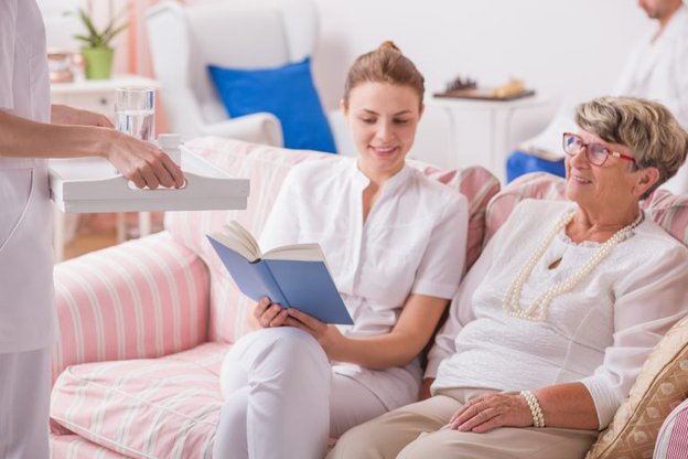 Realcare Health Service. Carer reading to lady on the sofa. 